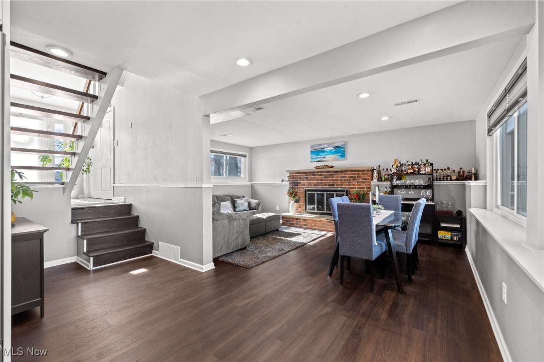 Open living and dining room with a brick fireplace, dark wood floors, and an open staircase.