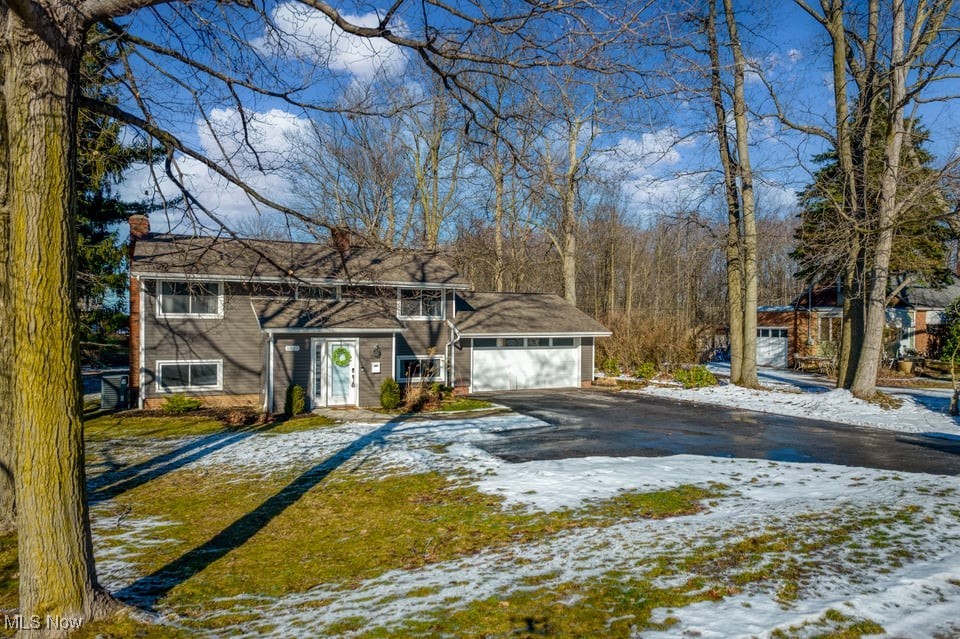 Gray two-story home with an attached garage, framed by bare trees and patches of snow.
