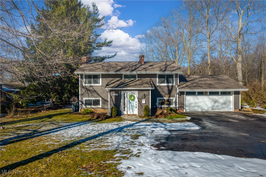 Gray split-level home with an attached two-car garage and snow patches across the front lawn.