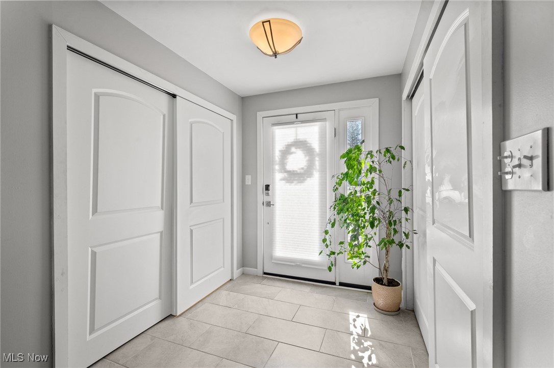 Entryway with a glass-paneled front door, tiled floor, and potted plant.