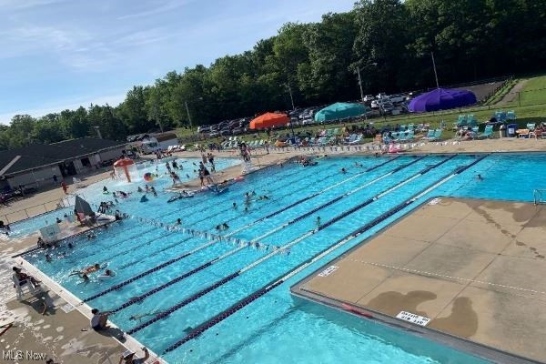 Outdoor lap pool with swimmers, a wet deck, and colorful shade canopies along the far side.