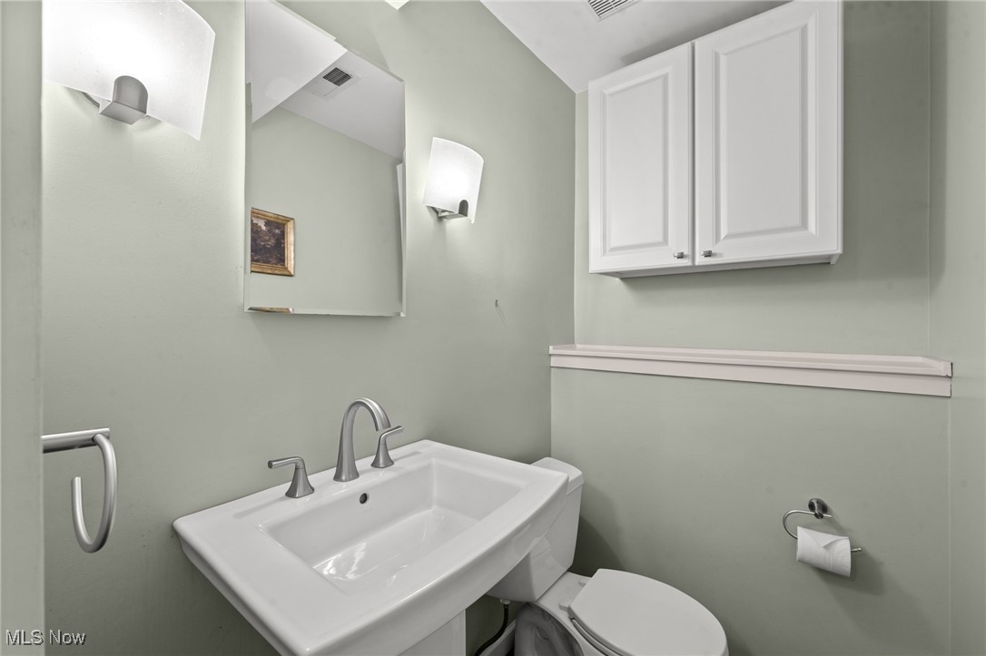 Bathroom with a white sink and toilet, mirrored cabinet, and pale green walls.