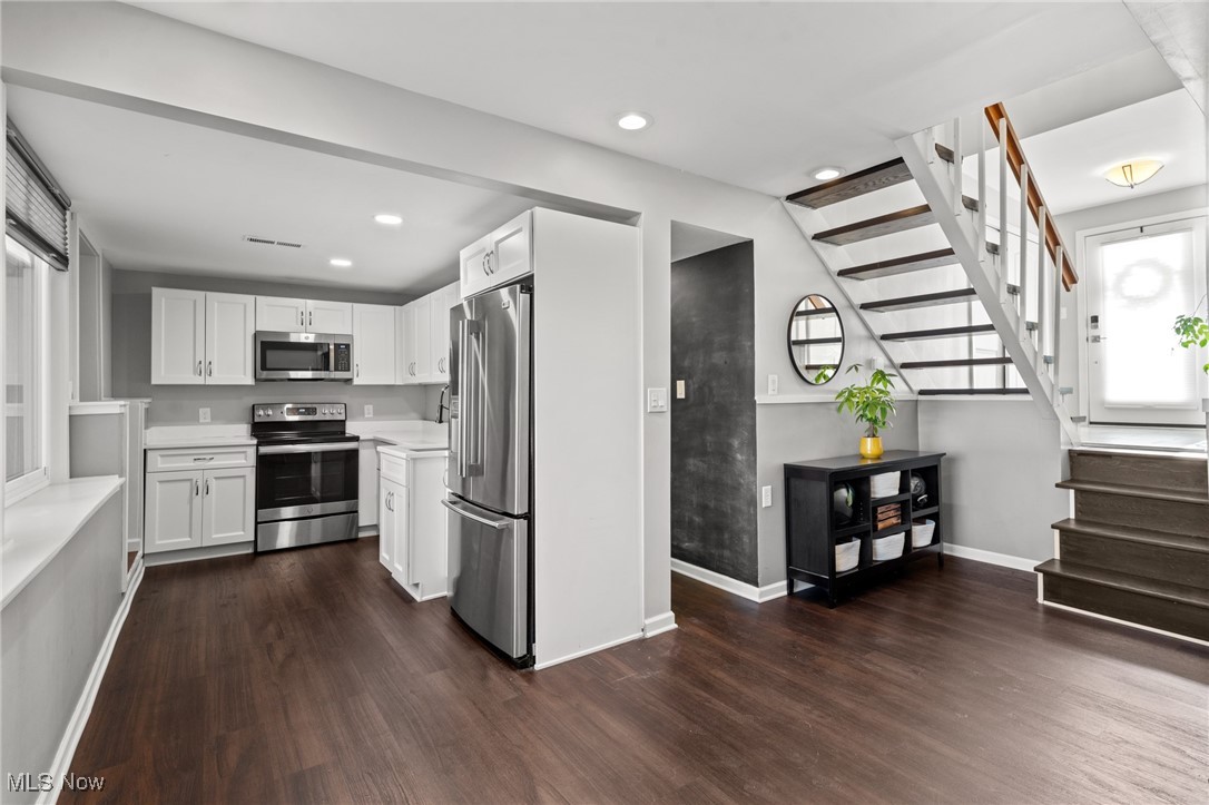 Kitchen with white cabinets and stainless appliances beside an open staircase with dark wood treads.
