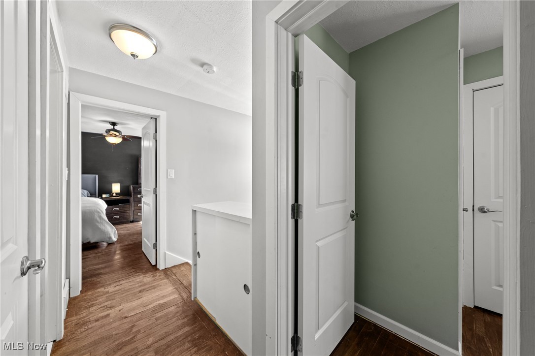 Hallway with hardwood floors and sage-green wall, looking into a furnished bedroom.