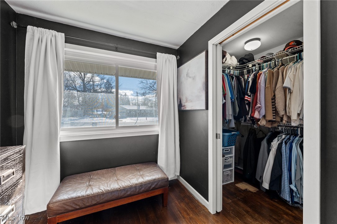 Bedroom dressing area with an open, clothes-filled closet and a leather bench by a snowy window.