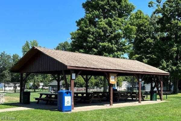 Covered park pavilion with picnic tables, a blue recycling bin, and surrounding trees.