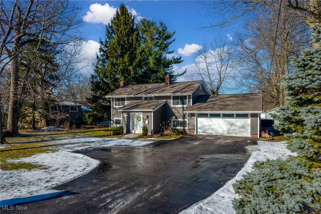 Gray two-story house with an attached white garage, broad driveway, and patches of snow.