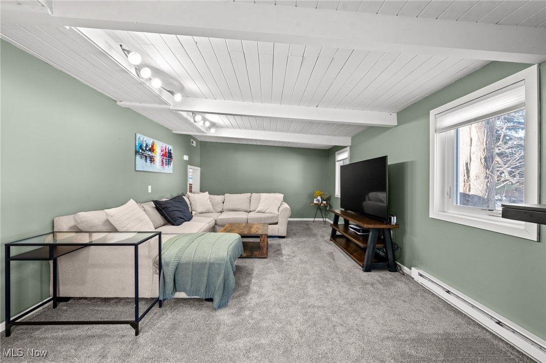 Living room with a cream sectional beneath a white vaulted ceiling and a television by the window.