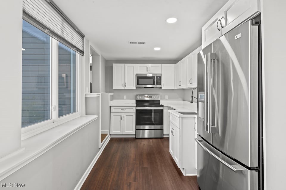 Kitchen with white cabinetry, stainless steel appliances, and dark wood flooring.