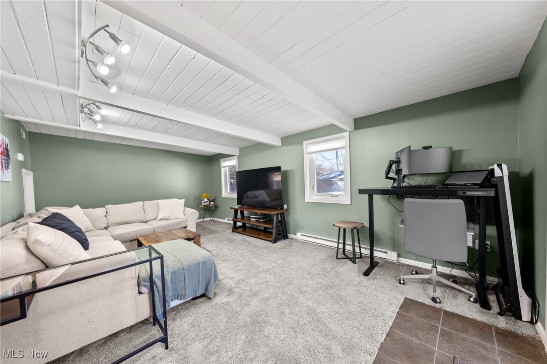 Living room with sage-green walls, white ceiling beams, a sectional sofa, and computer workstation.
