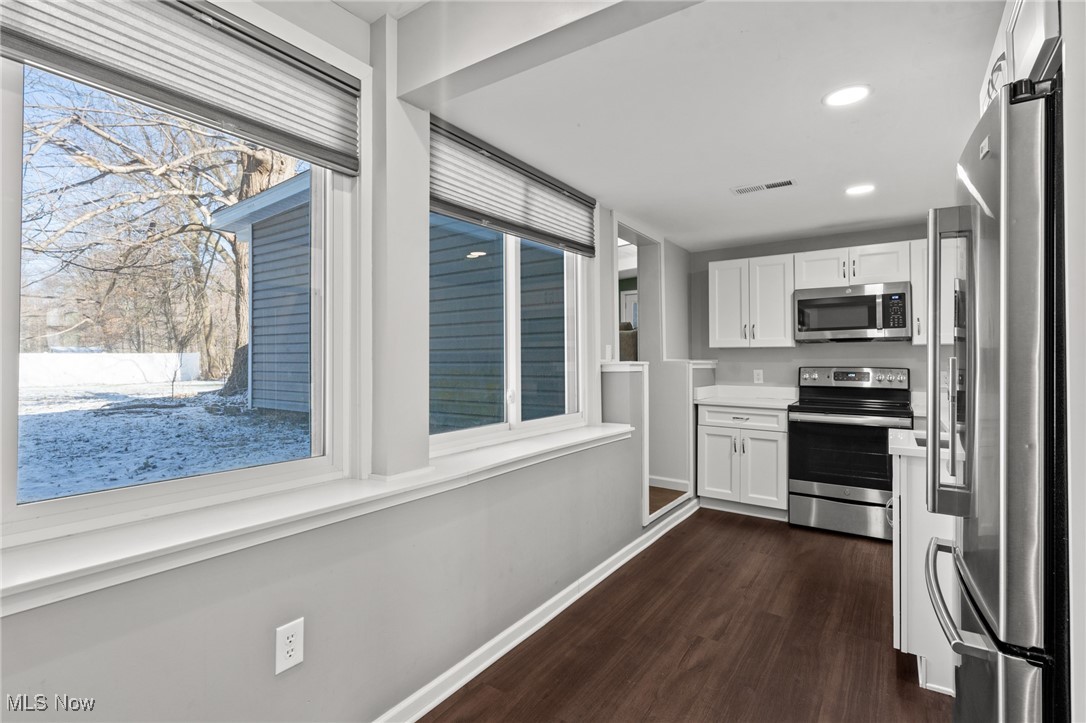 Kitchen with white cabinets, stainless steel appliances, and large windows overlooking a snowy yard.