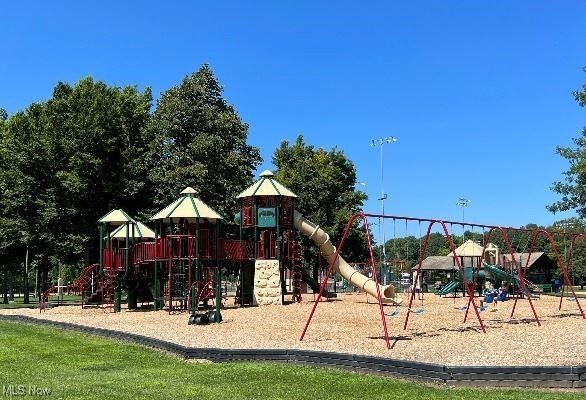 Community playground with a red-and-green climbing structure, slides, and swings on wood chips.