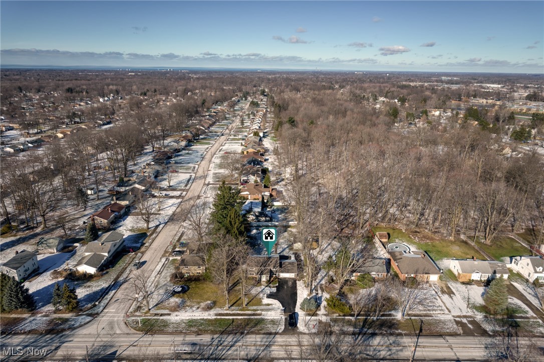 Aerial view of a marked home on a snowy, tree-lined residential street near the water.