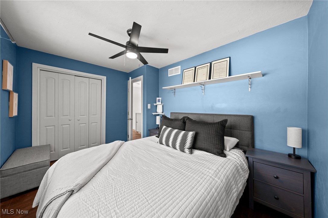 Blue bedroom with a gray upholstered bed, white quilted bedding, and a black ceiling fan.