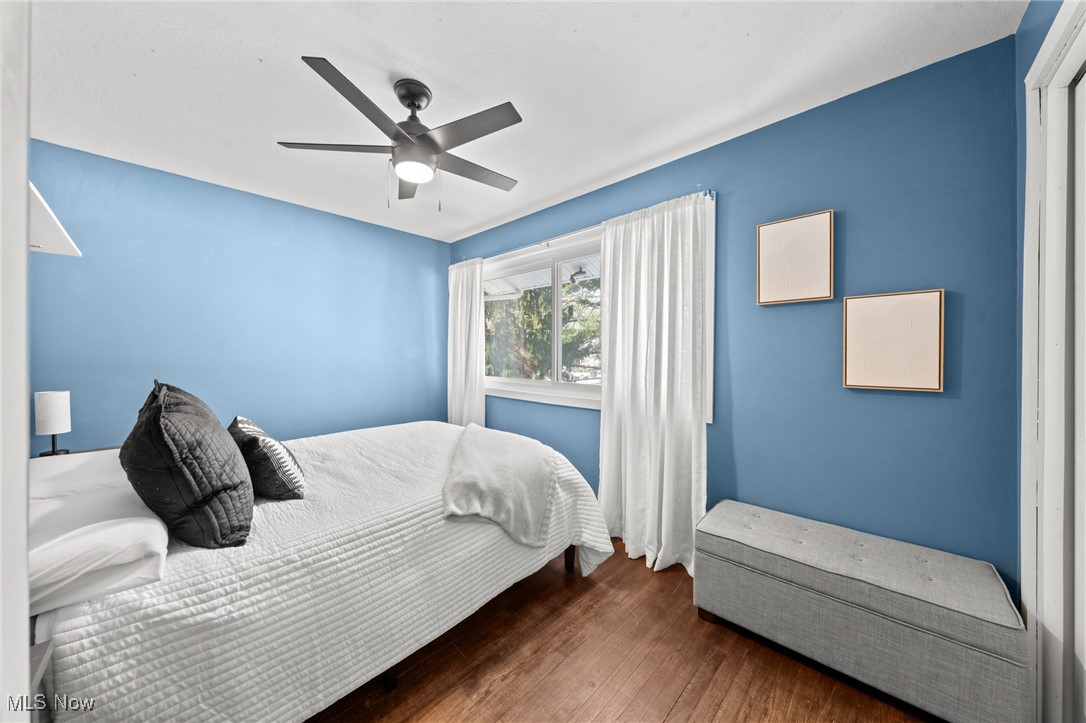 Blue bedroom with a white bed, curtained window, gray bench, and ceiling fan.