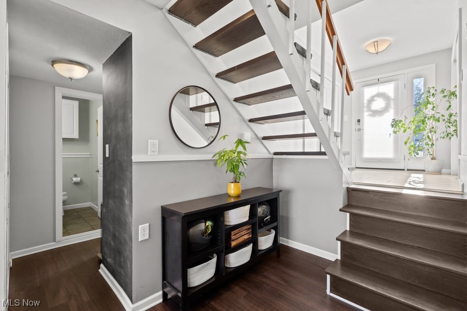 Entryway with an open-riser staircase, round mirror, console table, and bright front door.