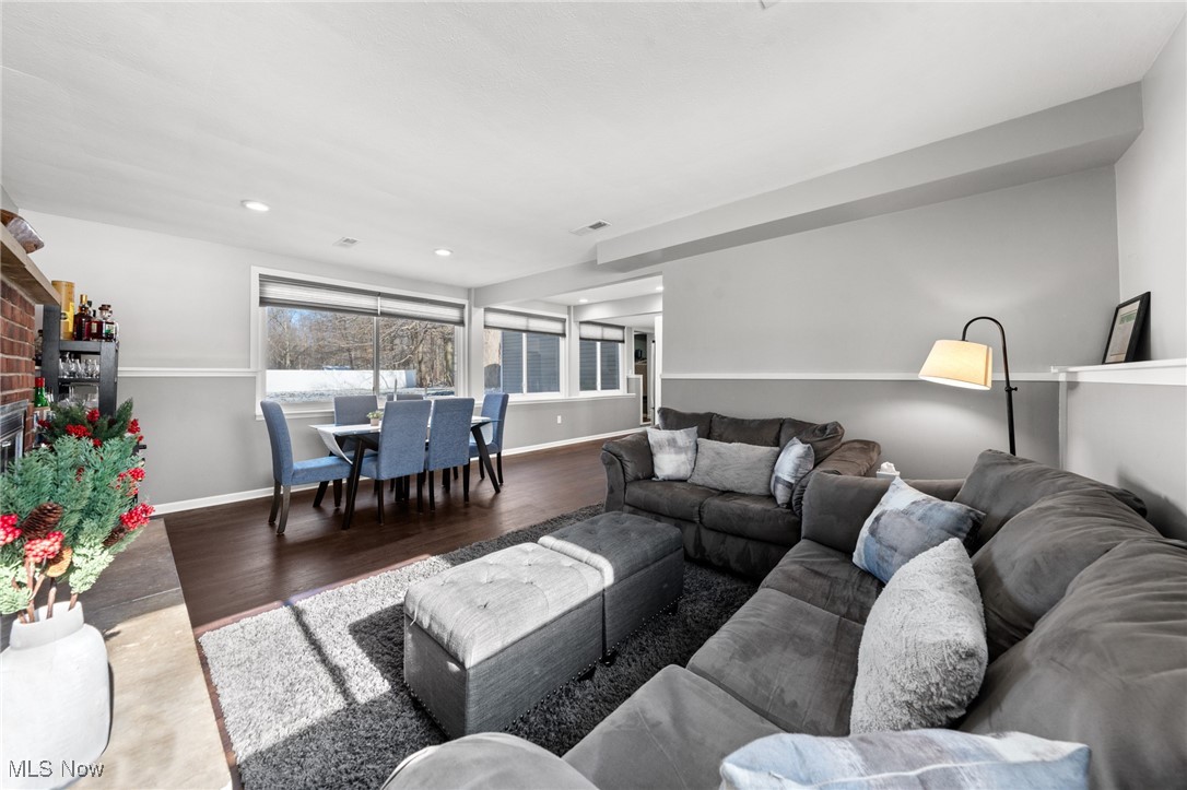 Living room with a gray sectional and ottoman beside a dining area with blue chairs and wide windows.