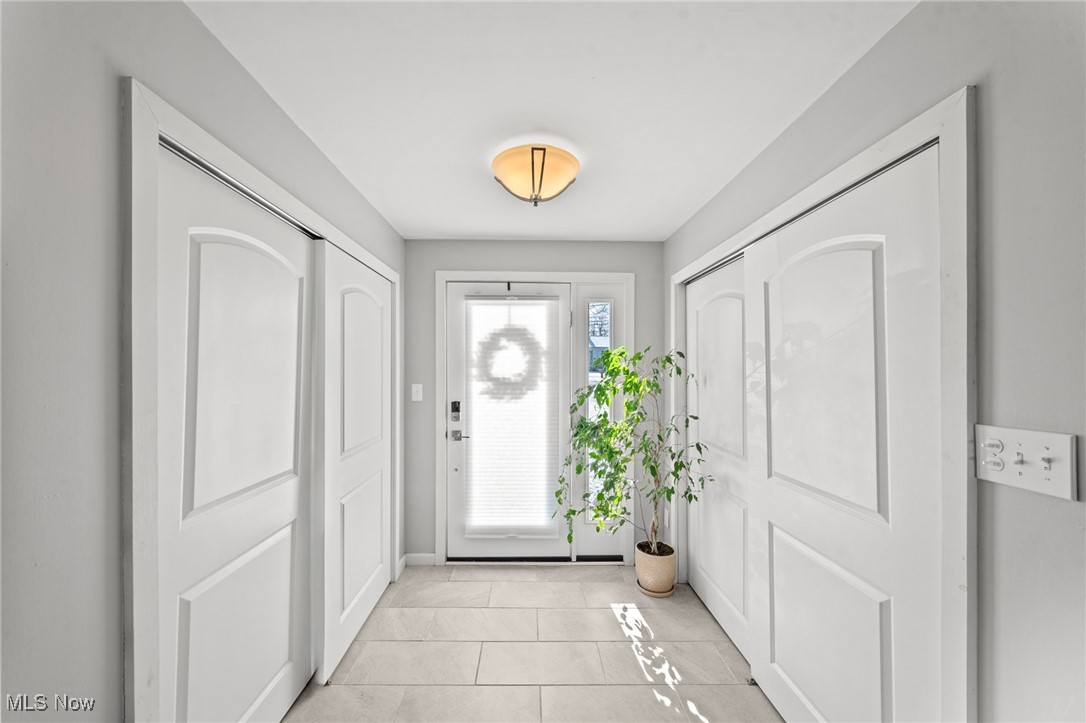 Bright tiled entry foyer with open white paneled doors and a potted plant beside the front door.