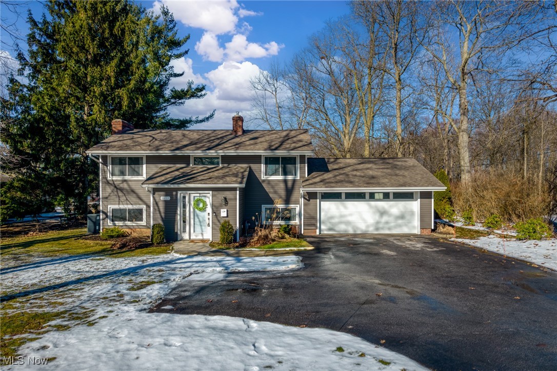 Gray two-story house with an attached garage, broad driveway, and patches of snow.