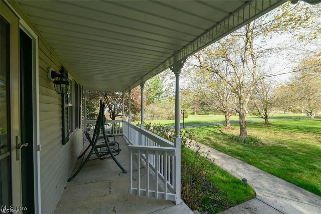 Covered front porch with a hanging swing overlooking a green lawn and budding trees.