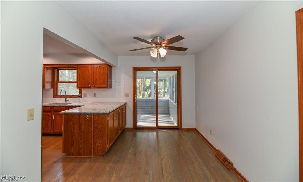 Empty dining area with hardwood floors, open to a wood-cabinet kitchen and enclosed sunroom.