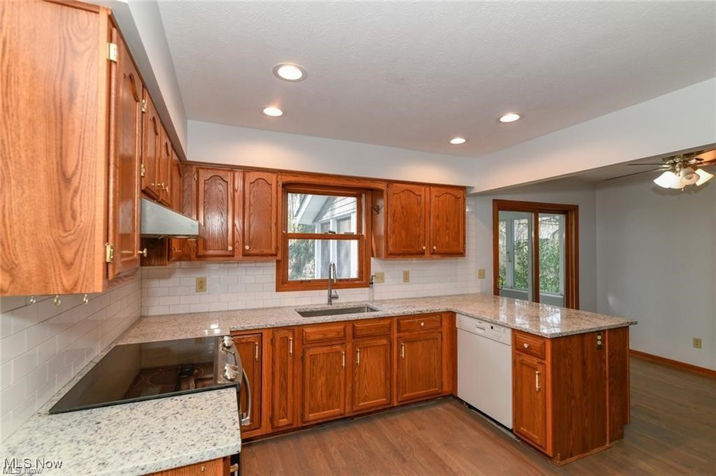 Kitchen with reddish wood cabinets, granite counters, a cooktop peninsula, and a sink beneath the window.