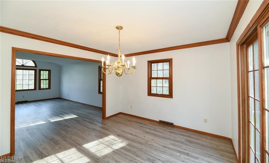 Vacant dining room with a brass chandelier, wood trim, gray flooring, and sunlit windows.