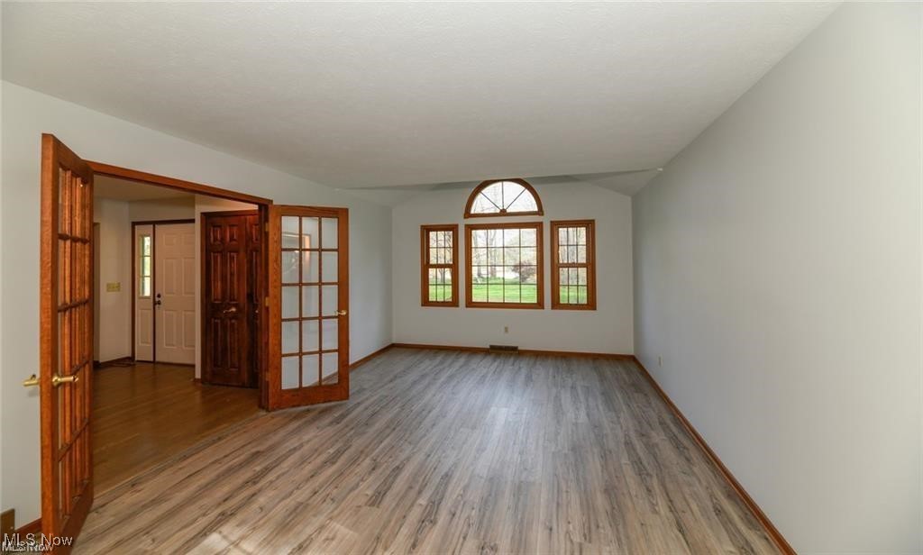Empty living room with gray wood-look floors, open French doors, and a large arched-top window.
