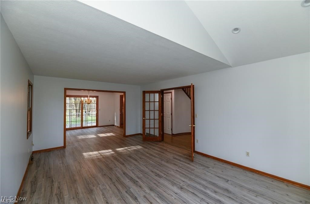 Empty living room with vaulted ceiling, gray flooring, and wood-trimmed openings to adjoining rooms.