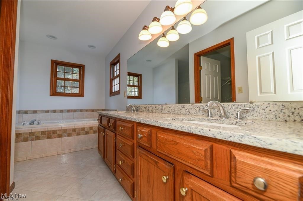 Bathroom with a long wood double vanity, granite counters, and a tiled soaking tub beneath windows.