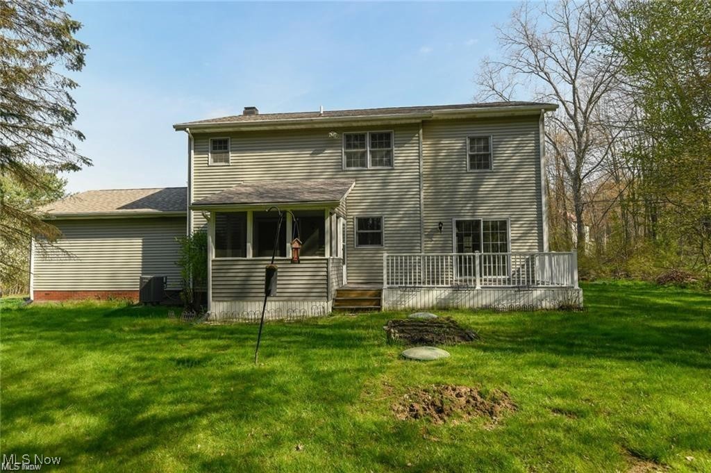 Rear exterior of a two-story gray house with a covered porch and raised deck overlooking a green lawn.