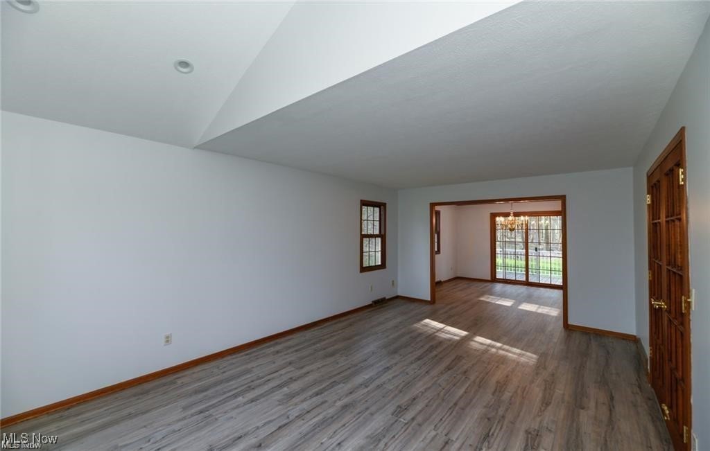 Unfurnished living room with vaulted ceiling, gray wood-look floors, and an adjoining room with sliding glass doors.