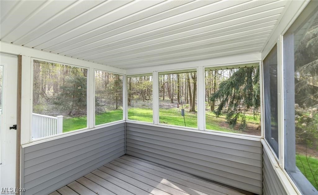 Enclosed porch with gray plank flooring and windows overlooking a wooded yard.