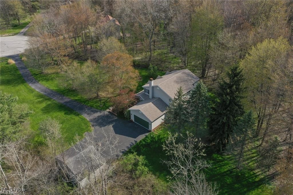 Aerial view of a two-story home with an attached garage and wooded grounds.