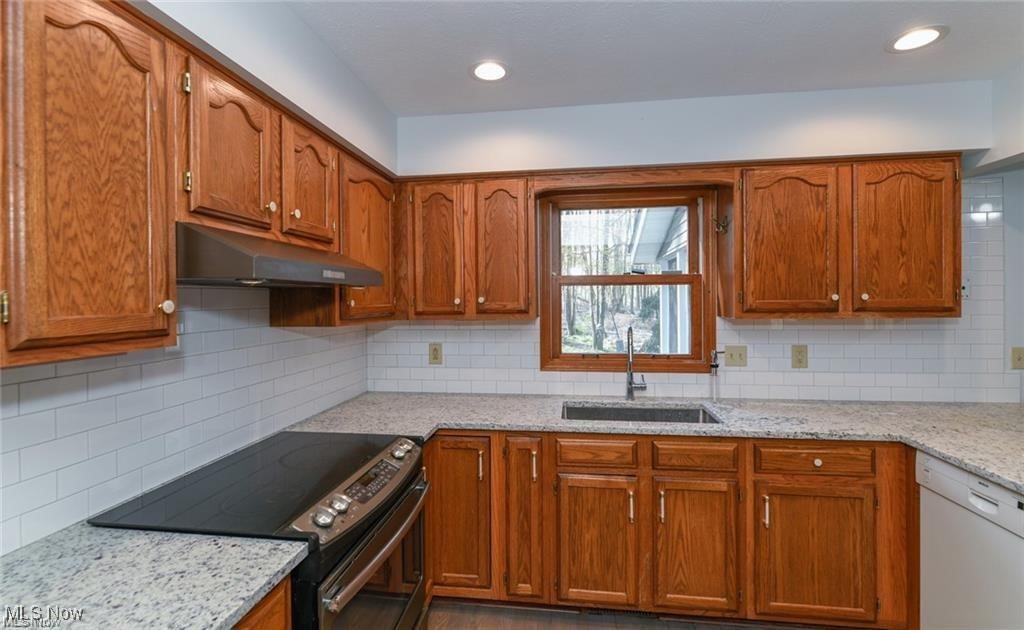 Kitchen with oak cabinets, granite counters, and a sink beneath a window overlooking trees.