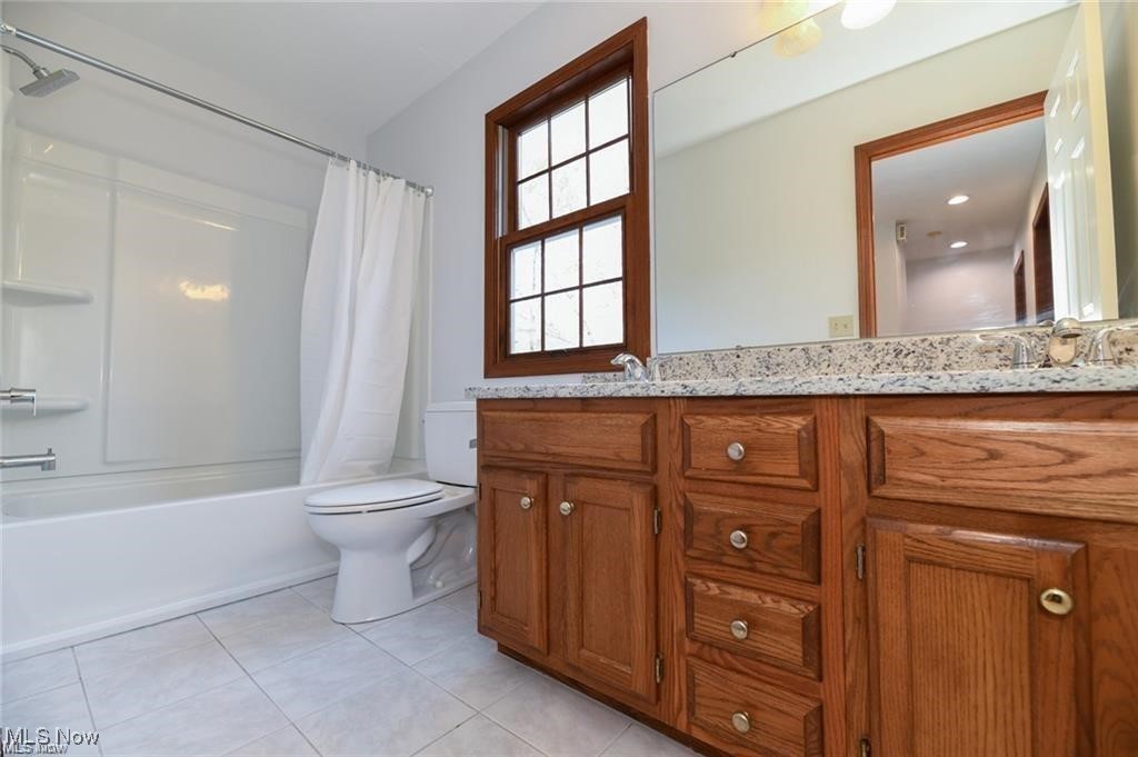 Bathroom with a white tub and shower beside a large wood vanity and wood-trimmed window.