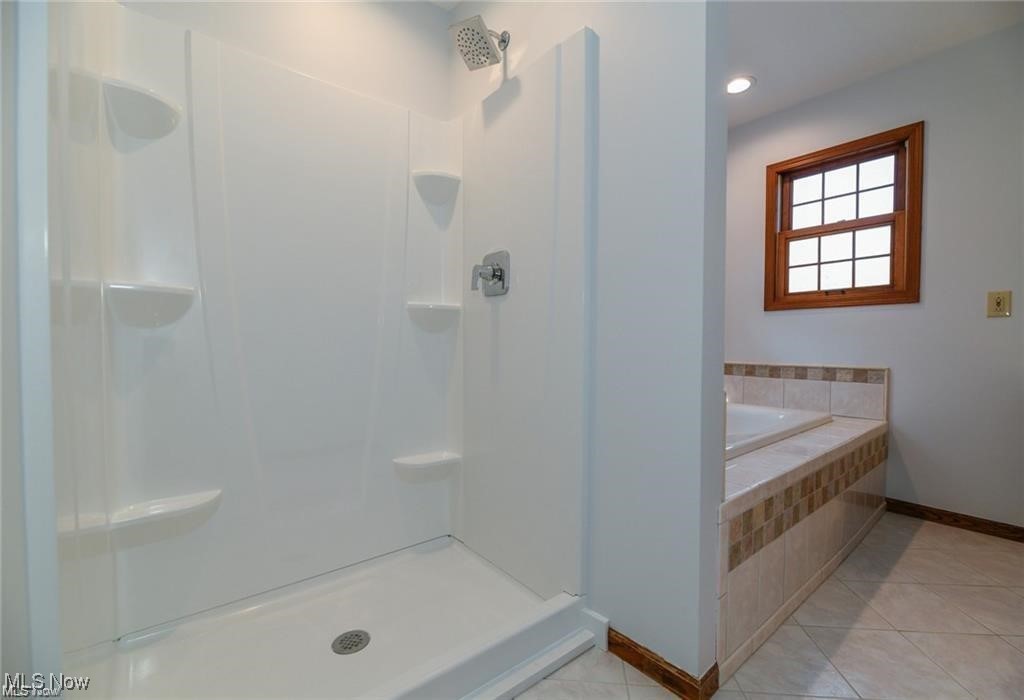 Bathroom with a white corner-shelf shower beside a tiled soaking tub and wood-trimmed window.