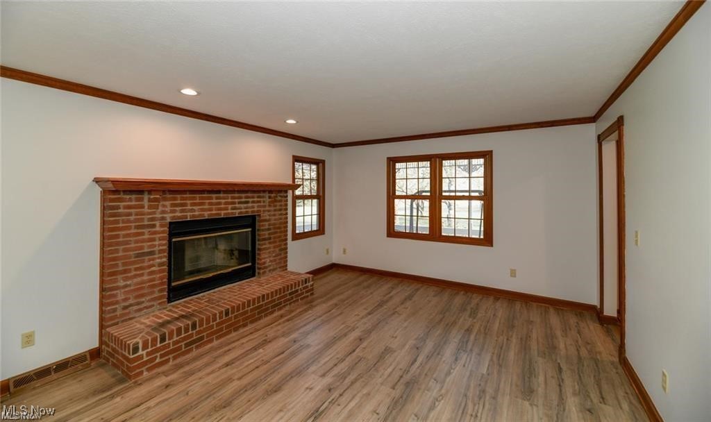 Empty living room with a brick fireplace, wood-look flooring, and wood-trimmed windows.