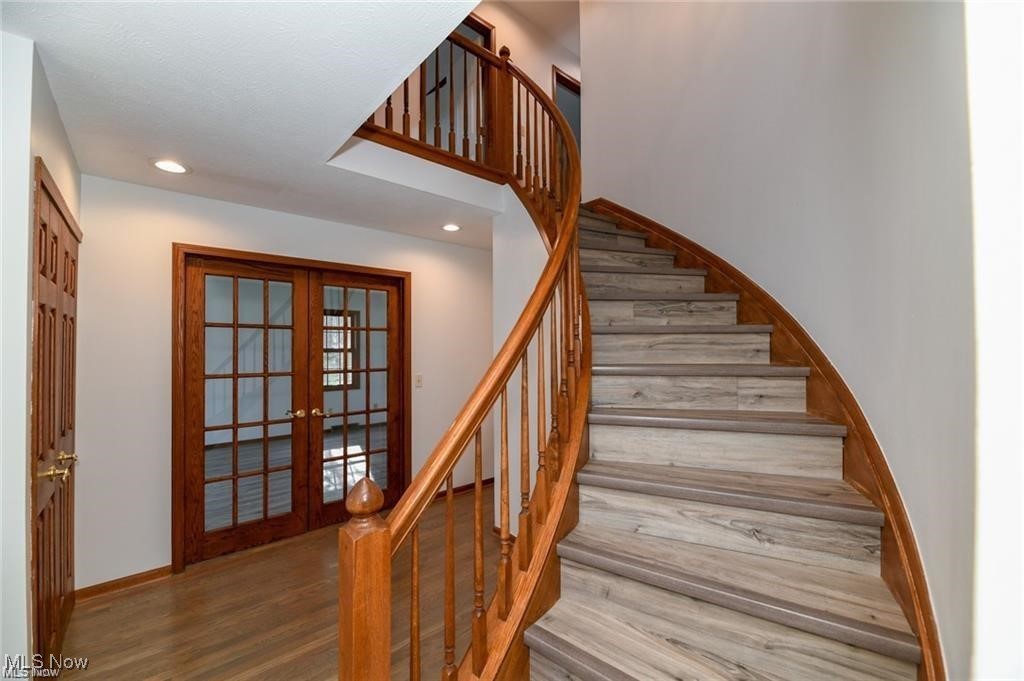 Foyer with a curved staircase, gray treads, wood railing, and wood-framed French doors.