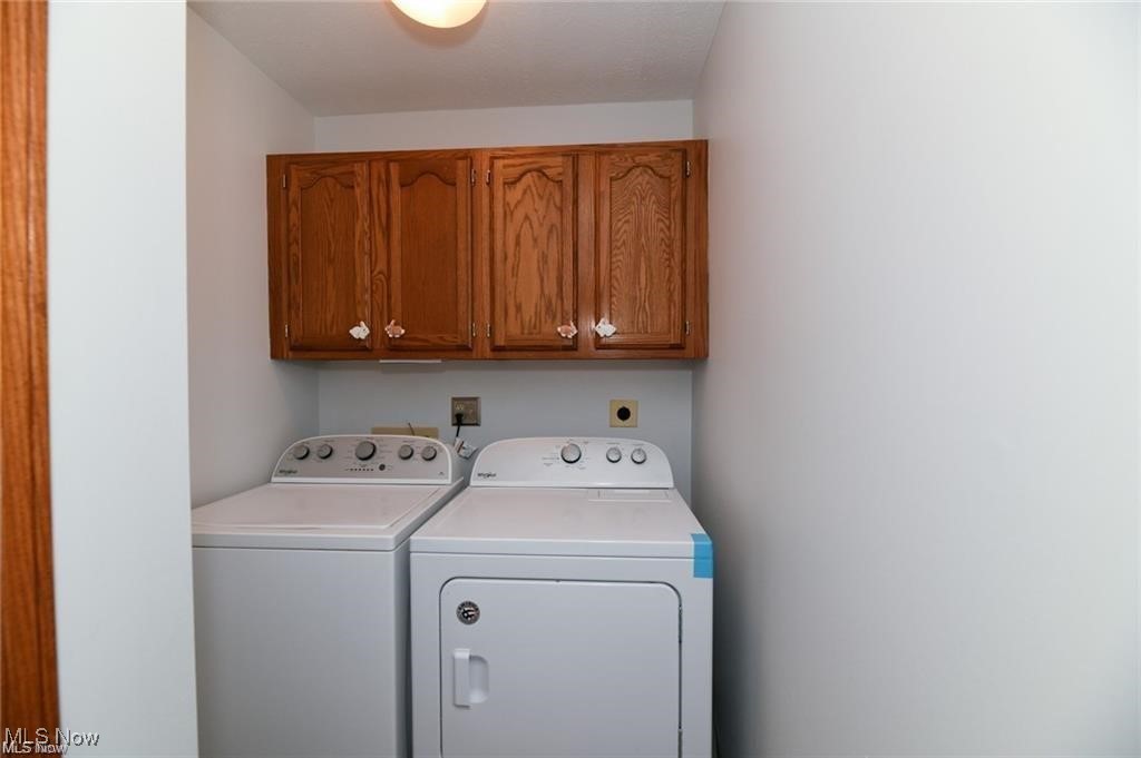 Laundry room with a washer and dryer beneath oak cabinets.