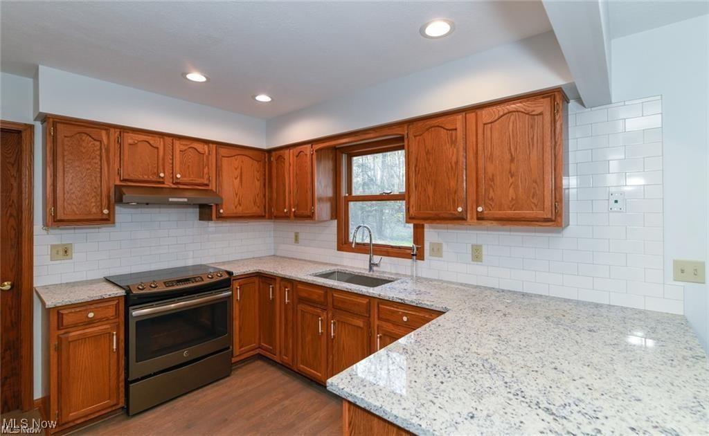 Kitchen with reddish wood cabinets, granite counters, and a sink beneath a window.
