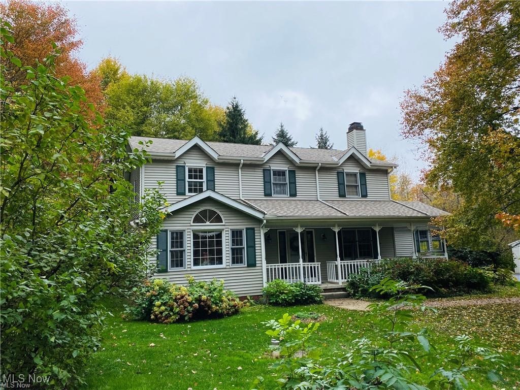 Two-story gray-sided home with a covered porch, dark shutters, and autumn trees.