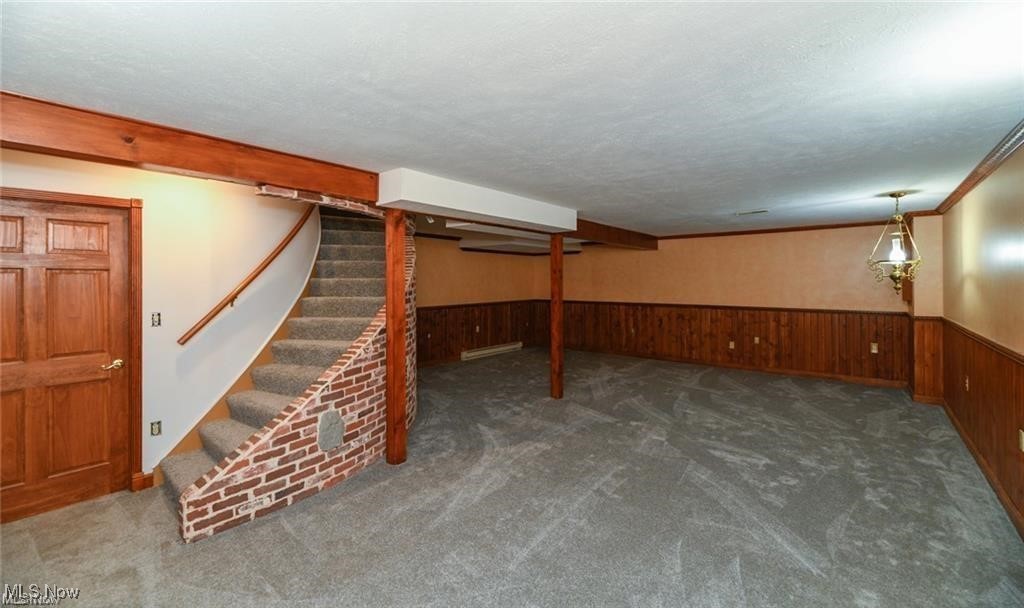 Empty basement recreation room with gray carpet, wood paneling, and a brick-edged staircase.