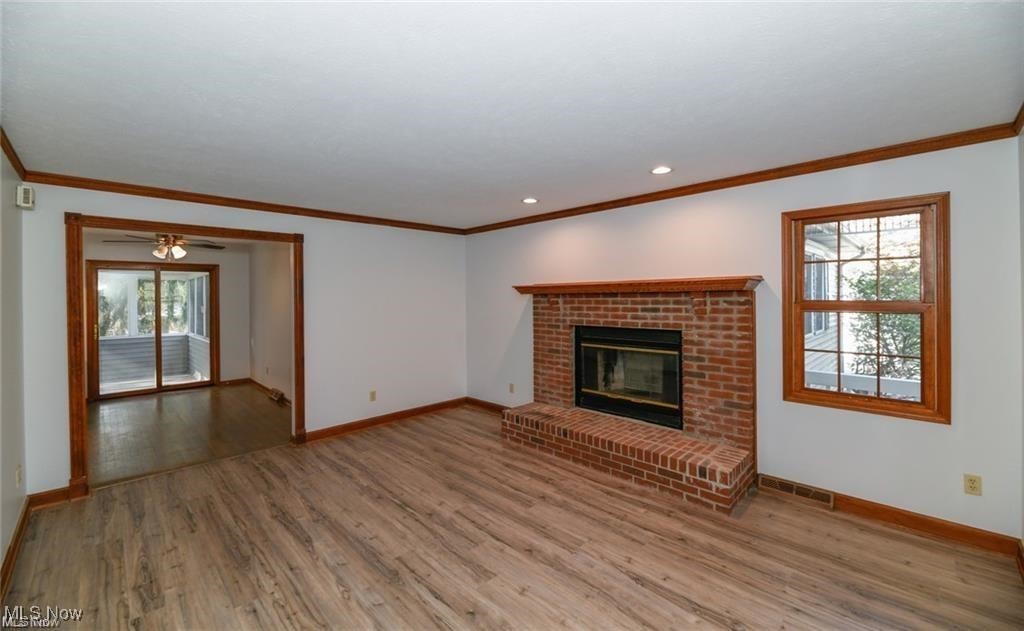 Empty living room with a brick fireplace, plank flooring, and a doorway to a sunroom.