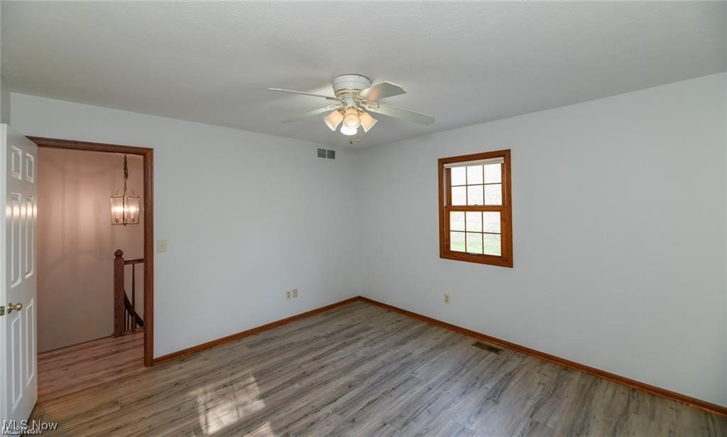 Empty bedroom with gray wood-look flooring, a wood-trimmed window, and a ceiling fan.