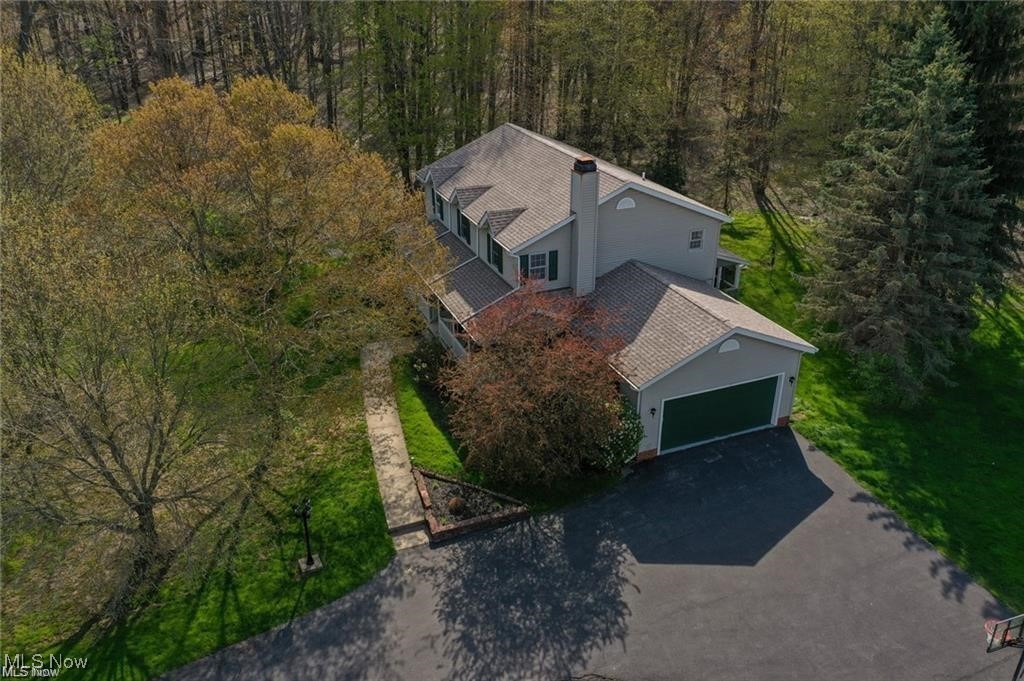 Aerial view of a gray two-story home with an attached garage, paved driveway, and mature trees.