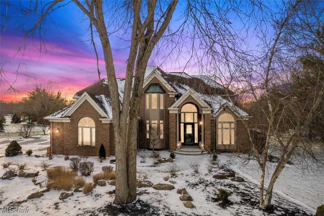 Brick home with arched entry and snow-covered landscaping beneath a vivid pink and purple dusk sky.