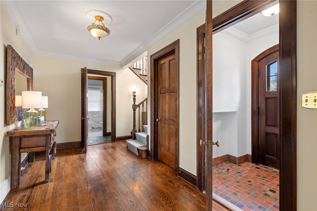 Foyer with hardwood floors, a wooden staircase, and an adjoining brick-floored entry.