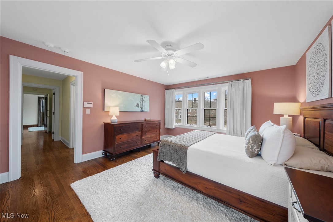 Bedroom with dusty rose walls, dark wood furniture, white bedding, and a wide curtained window.