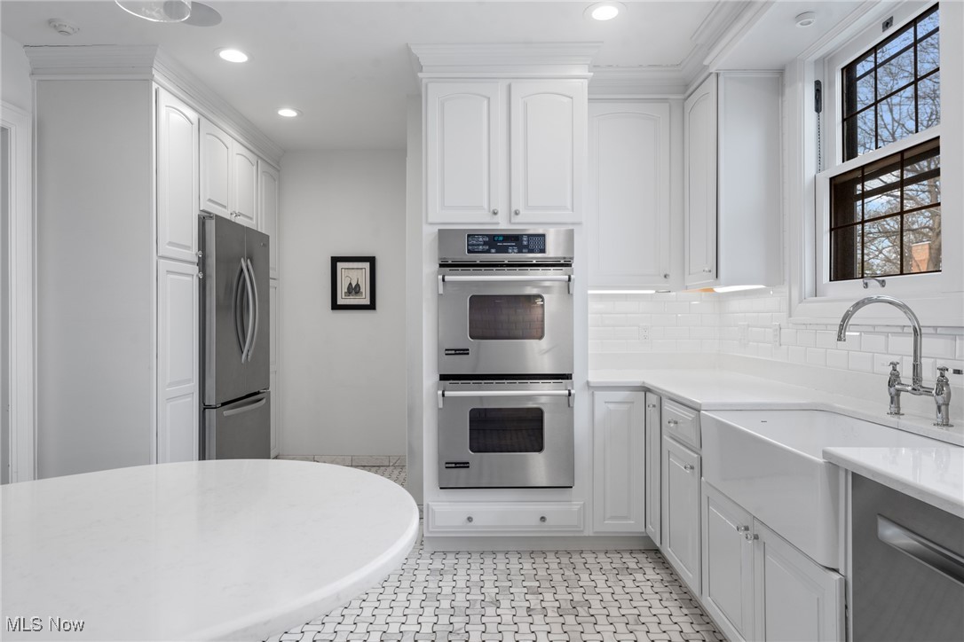 White kitchen with double wall ovens, farmhouse sink, rounded island, and patterned tile floor.